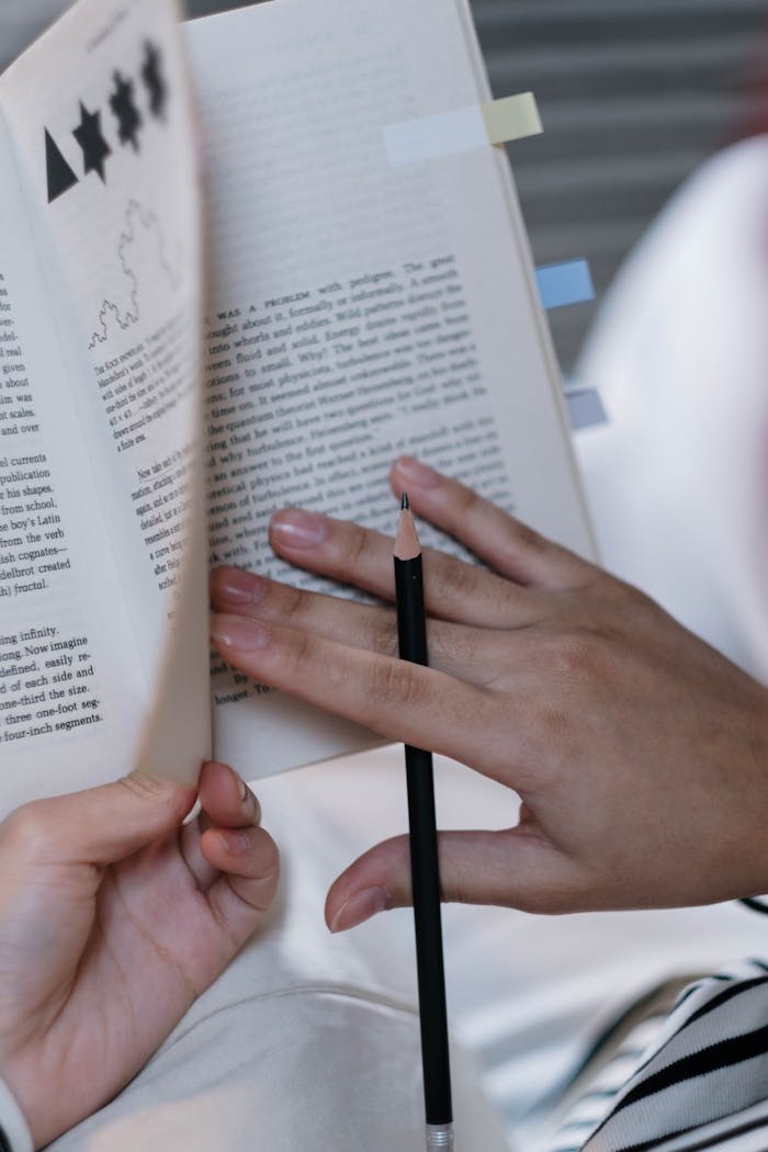 A close-up image of hands holding a pencil while reading a textbook, ideal for education themes.